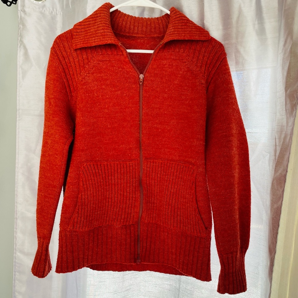 Woman’s orange zip up sweater has thumb holes 2 front pockets